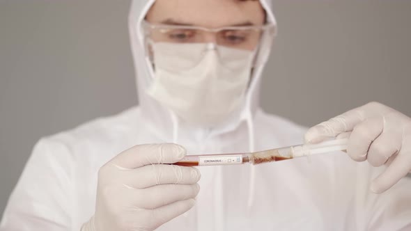 The Scientist in Full-covering Equipment Is Collocting Blodd From a Test with a Syringe