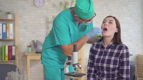 Man Doctor Taking a Saliva Test From a Young Woman's Mouth with a Cotton Swab Close Up