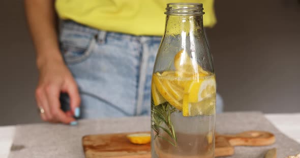 Female Hand Put Lemon in Glass Bottle Making Detox Healthy Water with Lemon and Rosemary