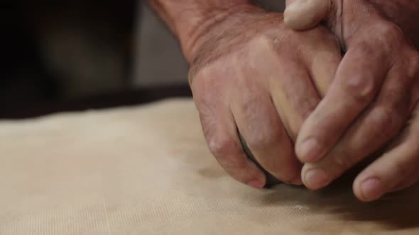 Male Hands Crumple and Roll Out Piece of Clay on Table Front View Closeup