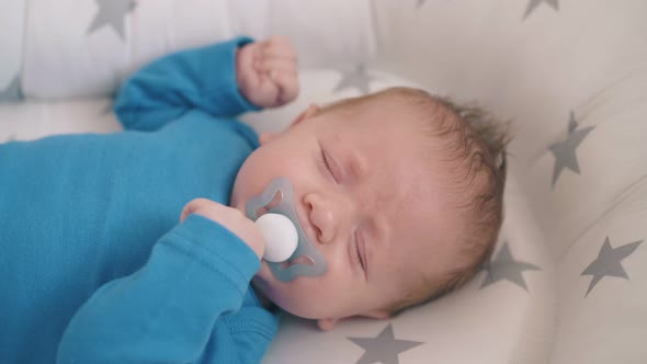 Cute Little Baby with Dummy Cries Sleeping in Cocoon in Crib