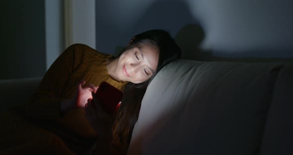 Woman use of mobile phone and sit on sofa at night