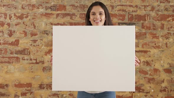 Caucasian woman holding a white rectangle on a brick wall