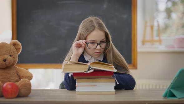 Curios Intelligent Teen Girl Reading Book Sitting at Desk in Classroom with Interested Facial