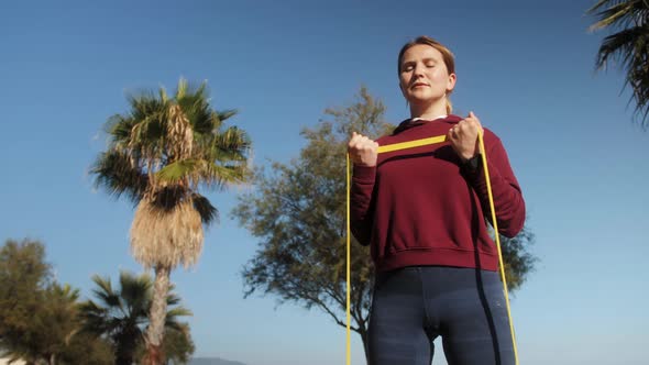 Beginner Sportswoman Training Outdoors on the Beach Embankment with Elastic Band Sport