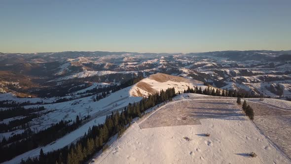 Aerial view of small village with scattered houses on snow covered hills in winter and bare dark 