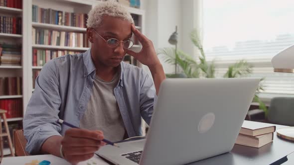 Puzzled African Man Rubs Temples Looking at Laptop Screen