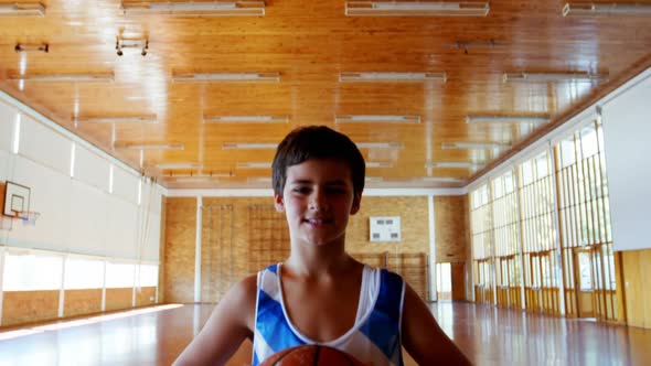 Portrait of schoolboy holding basketball in basketball court