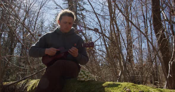 guy with tied hair in a ponytail plays the ukulele ukulele in the forest in autumn against