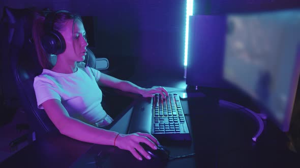 Young Concentrated Gamer Woman in Headphones Sits at the Computer in the Gaming Club and Playing