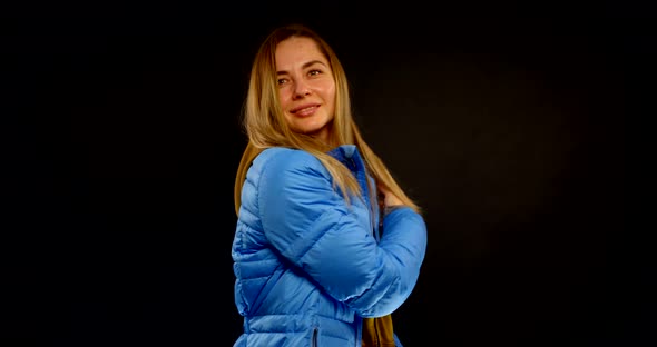 Portrait of a Blonde in a Hoodie and a Blue Jacket on a Black Background, the Girl Smiles