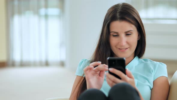 Young Business Woman Sitting on Couch and Using Smartphone