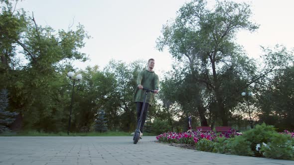 Caucasian Man Rides Electric Scooter Along Alley in Park