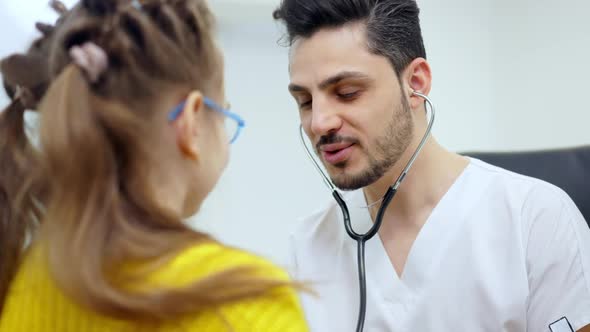 Portrait of Handsome Positive Pediatrician Listening Auscultation of Girl Using Stethoscope and