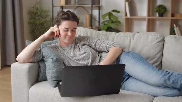 Calm Relaxed Young Attractive Woman Lying on Sofa with Laptop Share Messages Chat Online in Social