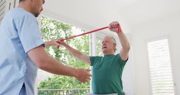 Male physiotherapist examining retired senior man exercising with resistance band at retirement home