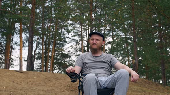 A Man Sits In The Woods On A Folding Camping Chair