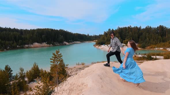 Young Happy Couple Running To a Sandy Hill and Looking at the Lake and Forest