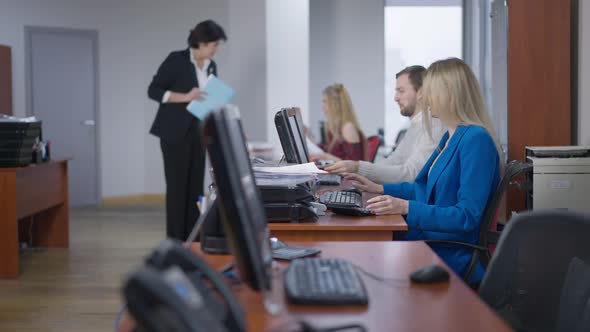 Side View of Blond Young Woman and Examining Documents As Blurred Serious CEO Talking with Employees