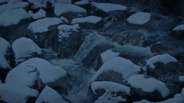 Snow Falls On Rocky River In The Evening