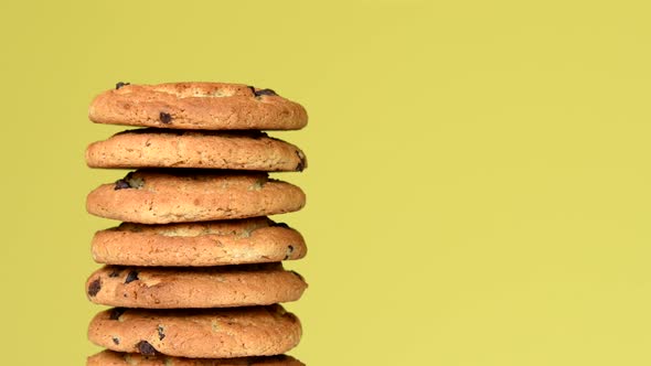 Pile of oat cookies with chocolate pieces rotating on yellow background
