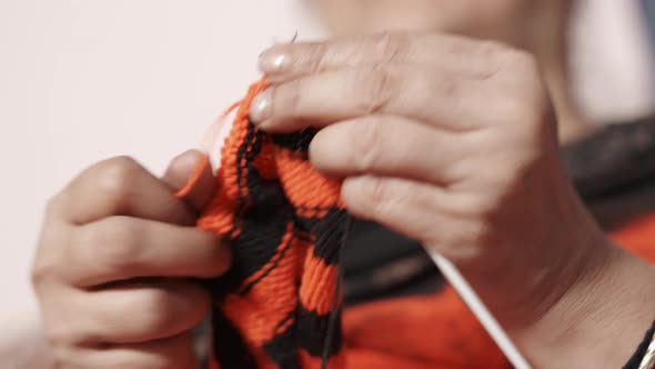 Indian woman knitting a scarf with red and black wool and two needle crafts. Close up of knit work t