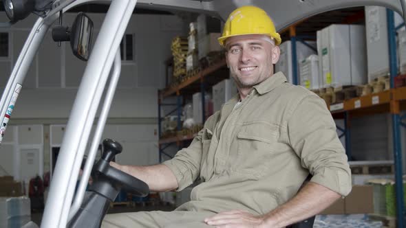 Cheerful Male Factory Worker Sitting in Forklift in Warehouse