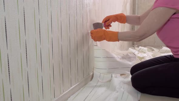 An Adult Woman Takes Off the Wallpaper Works with a Spatula in the Room