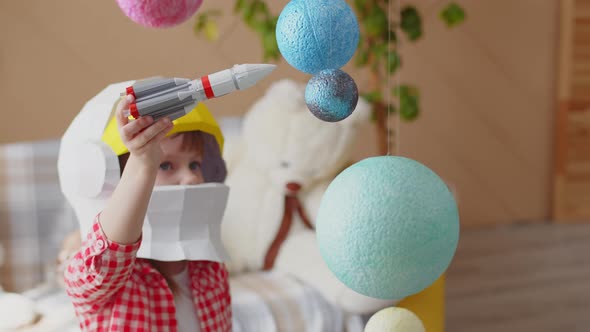 Boy child is playing with a rocket in a space helmet, sitting at home among the planets. alt