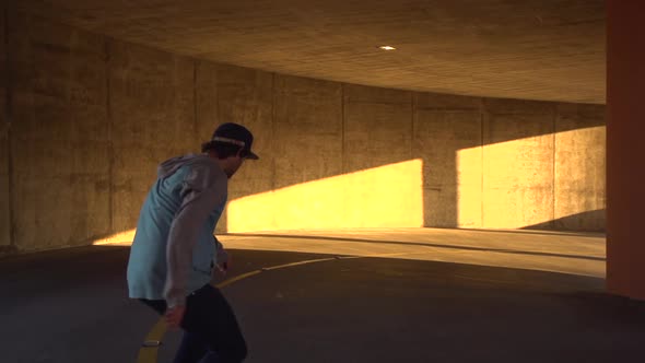 Silhouette of a young man skateboarding in a parking garage at sunset.