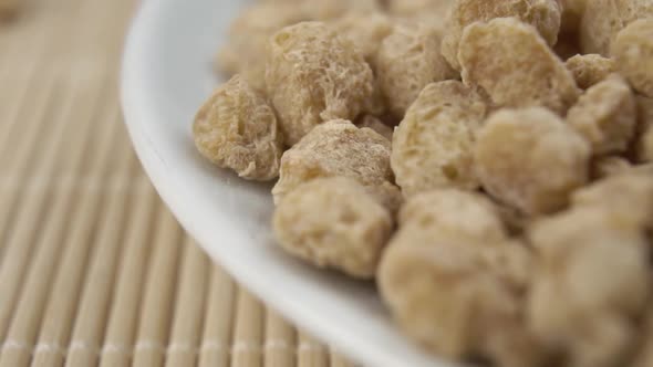 Uncooked dried soybeans close-up in a white bowl on a traditional bamboo mat