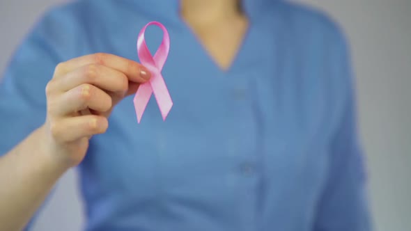 Female Physician Attaching Pink Ribbon to Coat, Breast Cancer Awareness Campaign