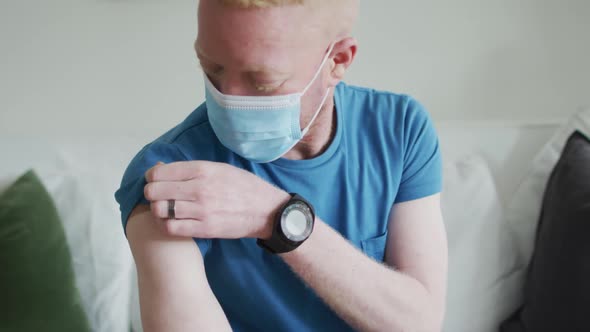 Happy albino african american man wearing face mask, with a plaster after vaccination