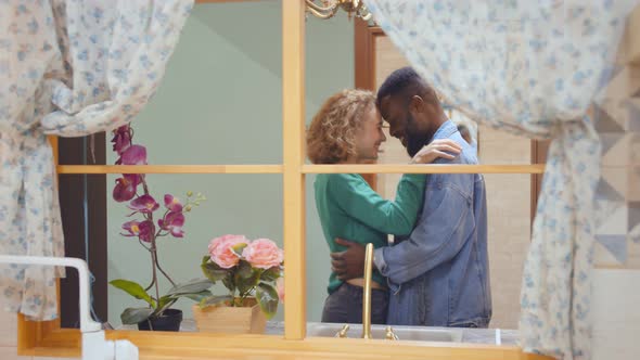 View Through Window of Lovely Diverse Couple Hugging Shopping in Modern Furniture Store