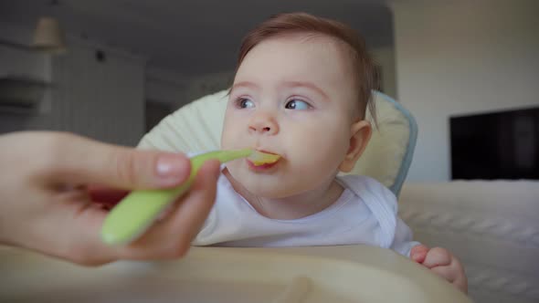 American Mother Feeding a Baby with a Spoon in Living Room Background