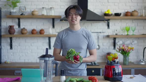 Smiling Asian Man Holding Radish and Salad Leaves Standing at Countertop Looking at Camera