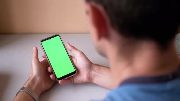 Man Holds a Smartphone with a Green Touchscreen on Table