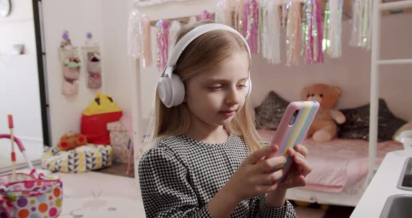 The 7Yearold Girl in the Children's Room with Headphones and Using Smartphone