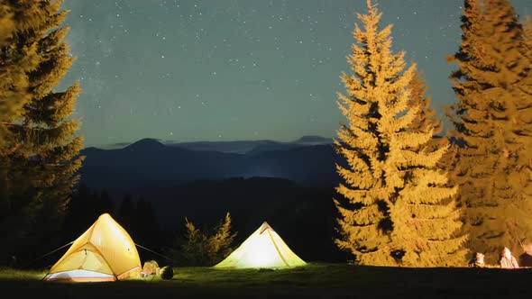 Timelapse of Hikers Resting Besides Bright Bonfire Near Illuminated Tourist Tents on Camping Site in