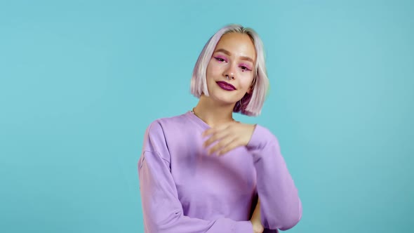 Pretty Woman with Unusual Colorful Purple Hairstyle Smiling, Flirting To Camera Over Blue Wall