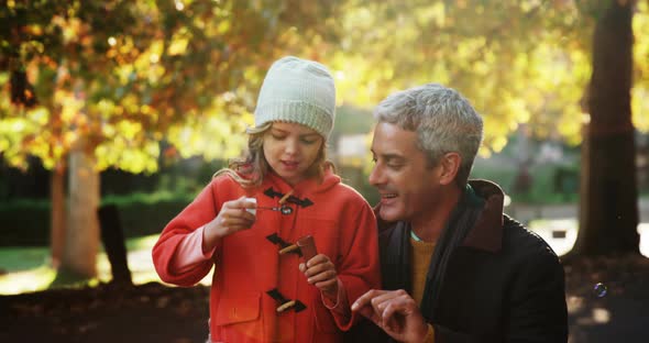 Girl blowing bubbles held by dad outdoors