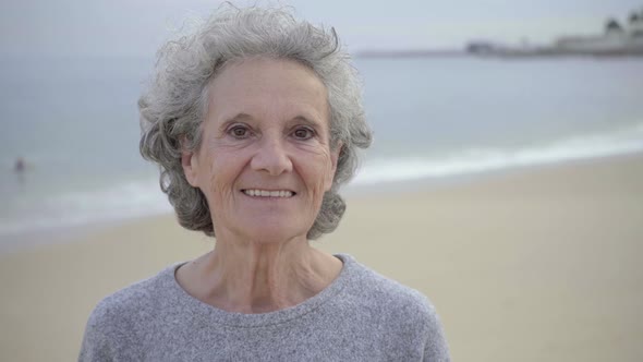 Happy Beautiful Elderly Woman with Toothy Smile Posing Against Blurred Seascape Background