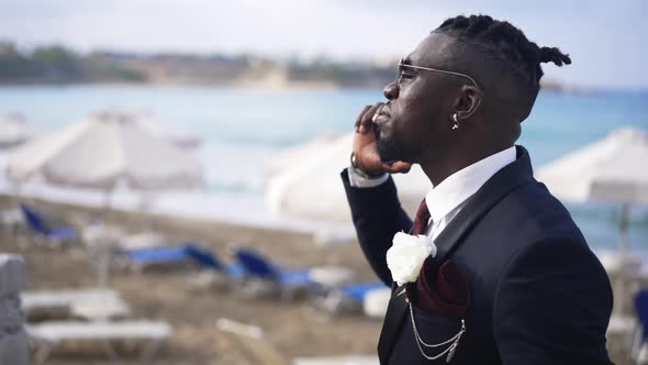 Angry African American Man in Elegant Suit Arguing on the Phone Standing on Resort on Sunny Day