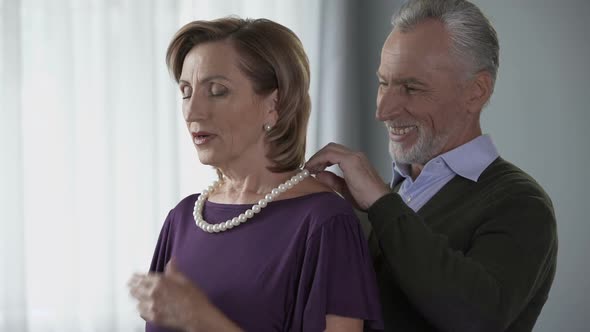 Elderly Man Putting Pearl Necklace on Wife and Kissing Her, Celebration, Present