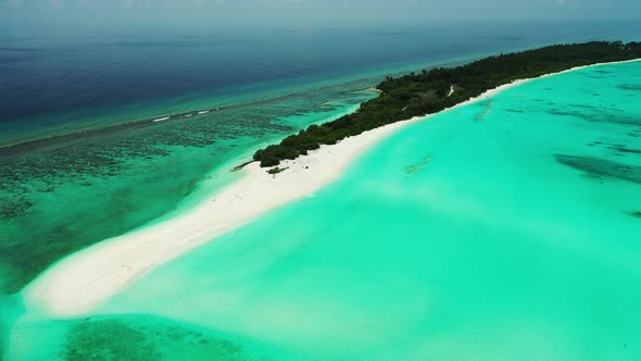 Long tropical island with dense green plants and wide white sandy beach located in the middle of tur