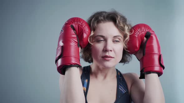 Young Beautiful Slim Woman Posing in Red Boxing Gloves in the Gym Against the Background of a Gray