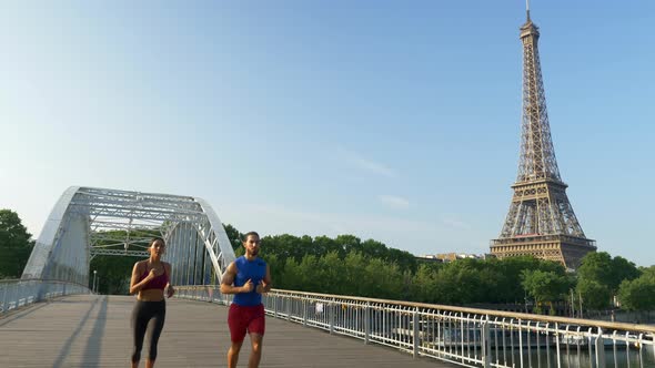 A man woman couple running across a bridge with the Eiffel Tower