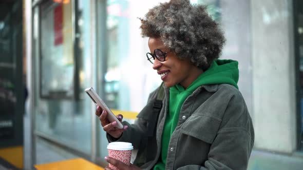 Positive adult African woman wearing casual clothes typing by phone