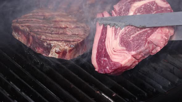 Searing and flipping ribeye steaks on grill