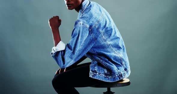 Androgynous man in denim shirt posing against colored background